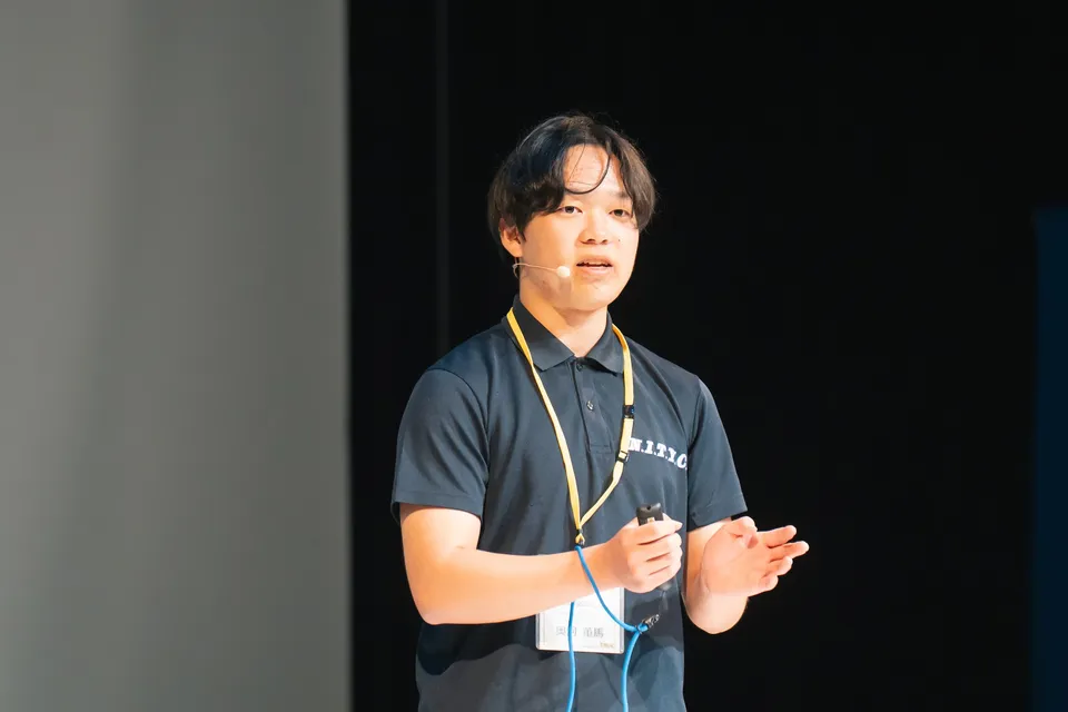 Close-up of Toma Okugawa speaking through a headset microphone in an N.I.T.Y.C. polo shirt during the Beacon pitch